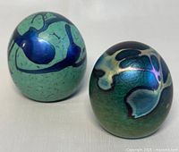 Two Robert Held art glass paperweights shown side by side on a white surface, highlighting the color and pattern on their surfaces.