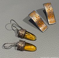Both pairs of vintage earrings shown together, highlighting yellow amber-colored drop earrings and rectangular orange enamel swirl design earrings.