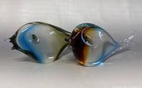 Side view of two hand blown glass fish paperweights side by side, showing their shape and color details.