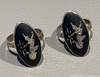 Pair of vintage sterling silver rings with black onyx elongated oval shape bezel featuring raised Manimekhala figures in silver.