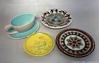 All four items displayed together on light surface: three decorative pottery plates and one ceramic gravy boat with underplate