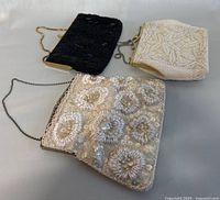 Shows three vintage evening bags with intricate beadwork and metal chain straps laid out flat.