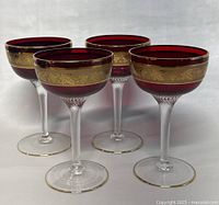 Four ruby red and gold goblets arranged in a group, showing side and top views of the decorative bands and textured clear stems.