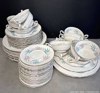 Overview photo showing stacked plates, cups, and serving platters with Lyric floral leaf pattern and silver trim.