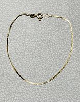Thin Italian 14K yellow gold bracelet with spring ring clasp, laid flat on textured surface.