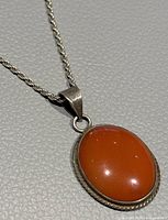 Close-up photo showing red carnelian oval pendant with twisted rope-edge bezel and silver bail on twisted rope design chain.
