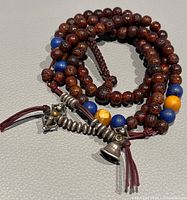 Full view of the lotus seed mala rosary coiled with visible blue and yellow accented beads and silver tassel charms.