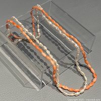 Necklace arranged on clear stand showing both pearl and coral strands.