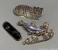 Front of three brooches: stylized cat, black enamel oval, gold-tone sleigh