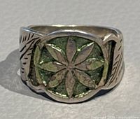 Close-up front view showing the ring face with green inlay and floral design on silver.