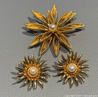 Brooch with flower shaped gold-tone leaves and central pearl, accompanied by matching clip-on sunburst earrings with pearl centers