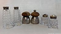 Front view of six vintage salt and pepper shakers, showing various shapes, glass cuts, and silver caps with wooden tops on two shakers.