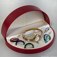 Watch and seven colored bezel rings displayed in red oval presentation case