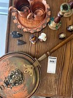 Photo of copper mugs on a round copper platter with scalloped edges, brass and wood candlesticks, glass salt and pepper shakers, and small decorative figures arranged on a wooden surface; part of the antique English brass bed warmer visible.