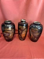 Photo of three Asian-inspired ceramic vases with black and gold mountainous landscape designs on a red backdrop.