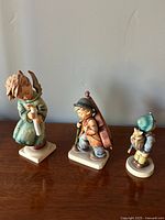 Three Berta Hummel collectible figurines displayed together against a white wall.