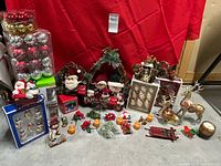Photo showing a variety of Christmas decorations including ornaments, wreaths, plush figurines, candle holders, and a gold reindeer figurine arranged against a red backdrop.