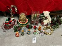 Photo of entire lot showing sled with plush toys, musical figurines, glass ornaments, white plush bear with foliage, pinecones, and gold ribbon
