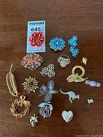 Top-down image of vintage costume jewelry brooches arranged on wooden surface, showing detailed designs and colors.