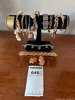 Full display of assortment of costume jewelry bracelets and earrings on black stand and flat surface.