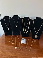 Ten gold tone chain necklaces with various pendants displayed on four black necklace holders and on a wooden surface.