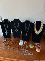 Photo showing four necklace displays: large turquoise cross pendant, delicate chains with small pendants, chunky gold-tone bib necklace and multiple necklaces laid on table with various pendants including purple, turquoise, and green stones.