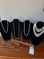 Wide shot showing all nine faux pearl necklaces displayed on three black necklace busts and laid on a wooden surface.