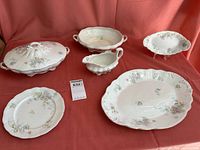 Full set displayed on red fabric showing all pieces: 1 shallow bowl, 1 gravy boat, 5 salad plates, 1 platter, and 1 vegetable bowl with lid.