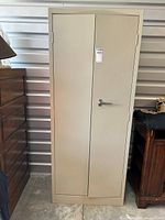 Closed view of the tall beige metal storage cabinet showing the double doors and lock handle.