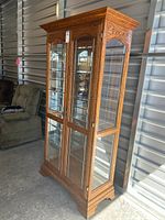 Full view of tall oak display cabinet with glass doors and sides, showing three glass shelves inside