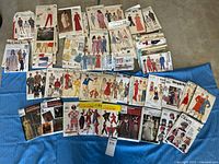 Overview photo showing a large collection of vintage sewing pattern envelopes spread on the floor, arranged to display front covers with illustrations of garment designs for men, women, and children.