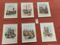 Six framed watercolor paintings of London landmarks laid out on table.