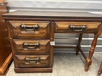 Full view of the wooden desk showing faux black leather top, four drawers with metal hardware on left and right side, turned legs, and wood grain finish.
