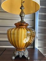 Close-up of one amber glass lamp body showing ribbed texture, amber color, and ornate metal base.
