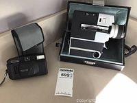 Pentax Mini Sport 35II camera with wrist strap and case next to Sankyo Super Cam 400 movie camera in its case.