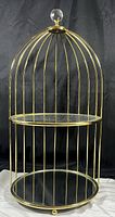 Front view of the gold-colored two-tier birdcage-shaped mirror display showing the vertical metal bars, mirrored shelves, and crystal top handle.