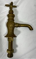 Side profile of brass faucet showing detailed bamboo and leaf pattern engraving on the body and base, with curved spout and cross handle.