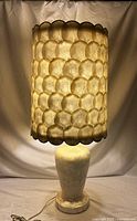 Illuminated full view of vintage capiz shell table lamp showing the lamp body and scalloped shell shade with brass accents at edges.