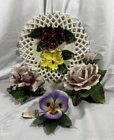 Front view photo of entire lot showing the vintage open lattice ceramic wall plate with red and yellow floral relief by Silvia Ceramics California, two pink Capodimonte roses, and Capodimonte pansy ceramic flower with tag