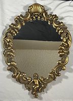 Full front view of the ornate oval mirror showing gold cast plaster frame with cherubs and shell motif