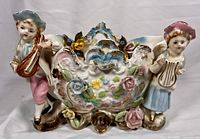 Front view of the porcelain basket showing boy and girl figurines, floral details, and gold accents.