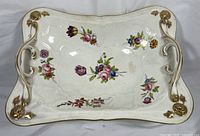 Top-down view of porcelain centerpiece basket bowl showing floral patterns in pink, purple and blue with gold rim and handles.