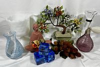 Full lot view showing various glass and collectible decorative items including crystal holder, bonsai tree, sculpture, grapes, and blue glass cubes.