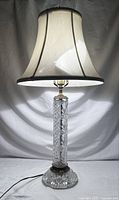 Full view of the lamp lit, showing cut crystal column, fabric shade, and overall height and shape