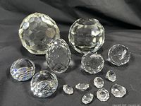 Overview of the 15 faceted clear crystal pieces including various orbs, tear drop shapes, egg shape, and small loose crystals arranged on a black surface.