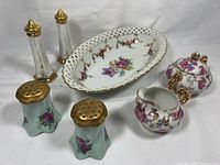 Set of vintage porcelain items including salt and pepper shakers, creamer, sugar bowl, and oval dish with floral and gold trim designs.