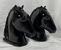 Close view of two black ceramic horse head bookends showing high gloss finish and sculpted details. One piece has a visible crack and repair.
