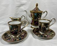 Whole tea set featuring teapot, creamer, two cups, two saucers with detailed hand-painted classical courting figures and gold trim.