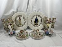 Overview of collection showing Lord Nelson plates with figures, Arnart wall plaques, and both pairs of ceramic candle holders with floral themes.