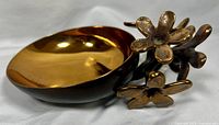 Angled side view showing the polished brass bowl and detailed flower base, highlighting the reflective surface and floral design.
